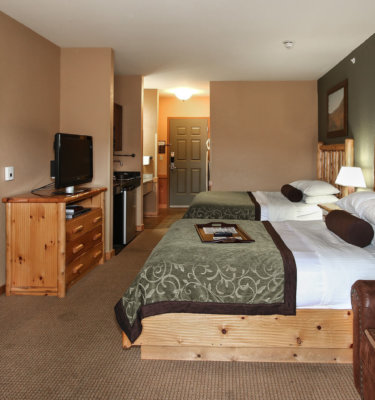 A hotel room with two beds, a kitchenette, and a TV