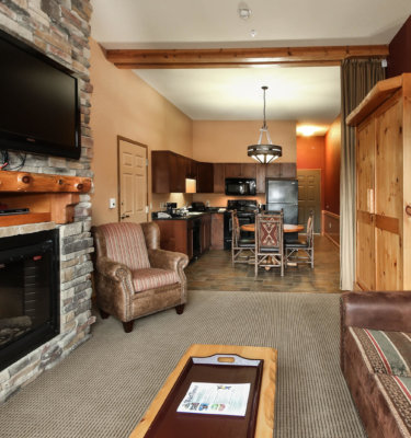 A wide view of a hotel suite's living area, showing a stone fireplace, kitchenette, and dining area.