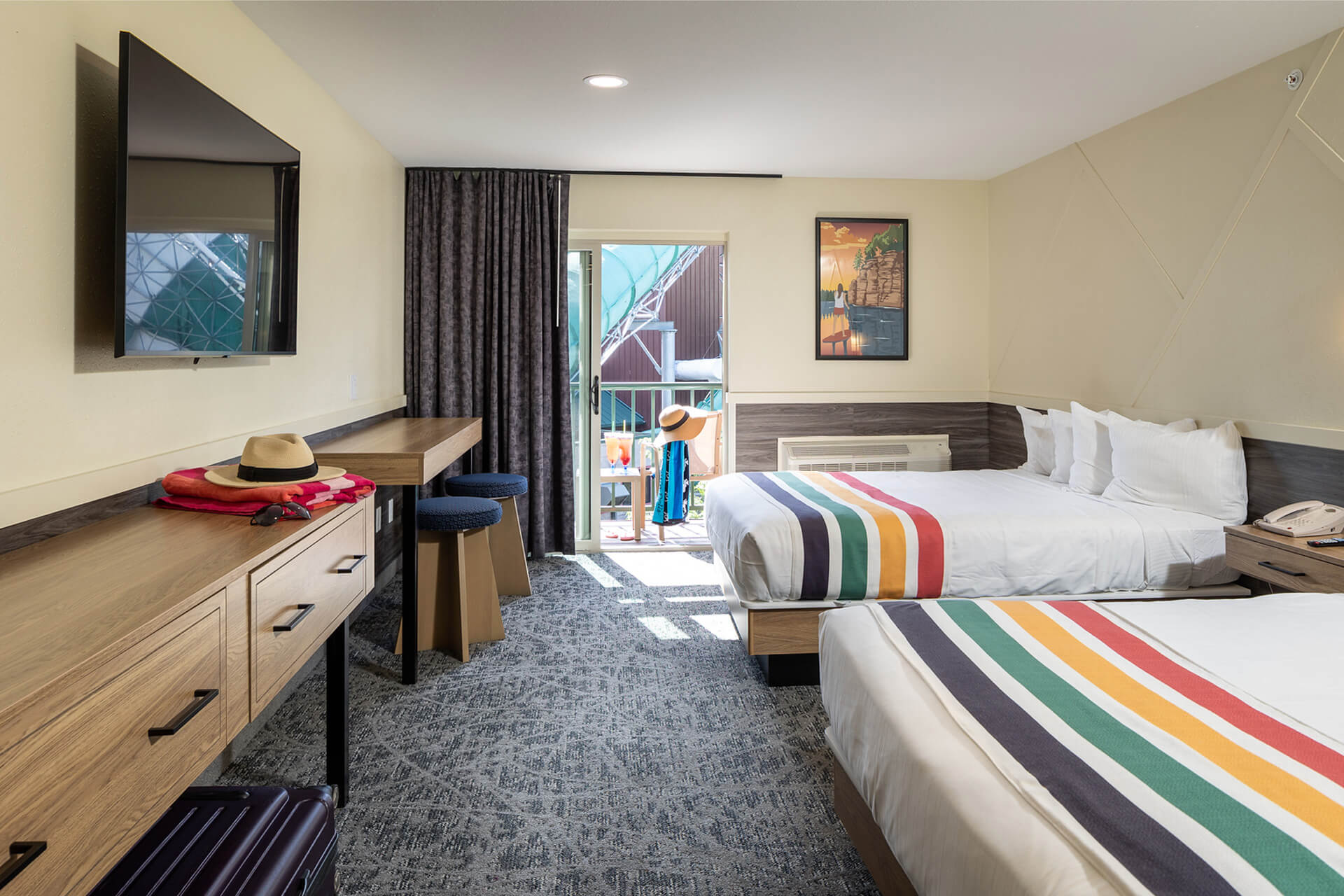 A hotel room with two queen beds, a balcony, and a desk with a TV.