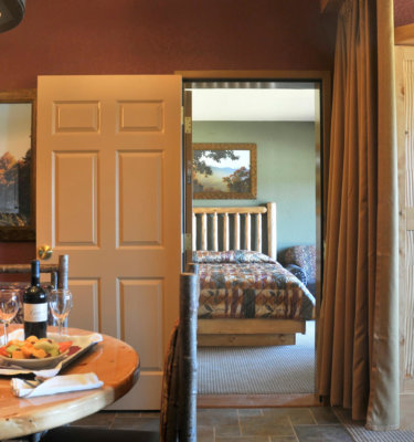 A room with a table and wine glasses in the foreground, and a bed in the background.