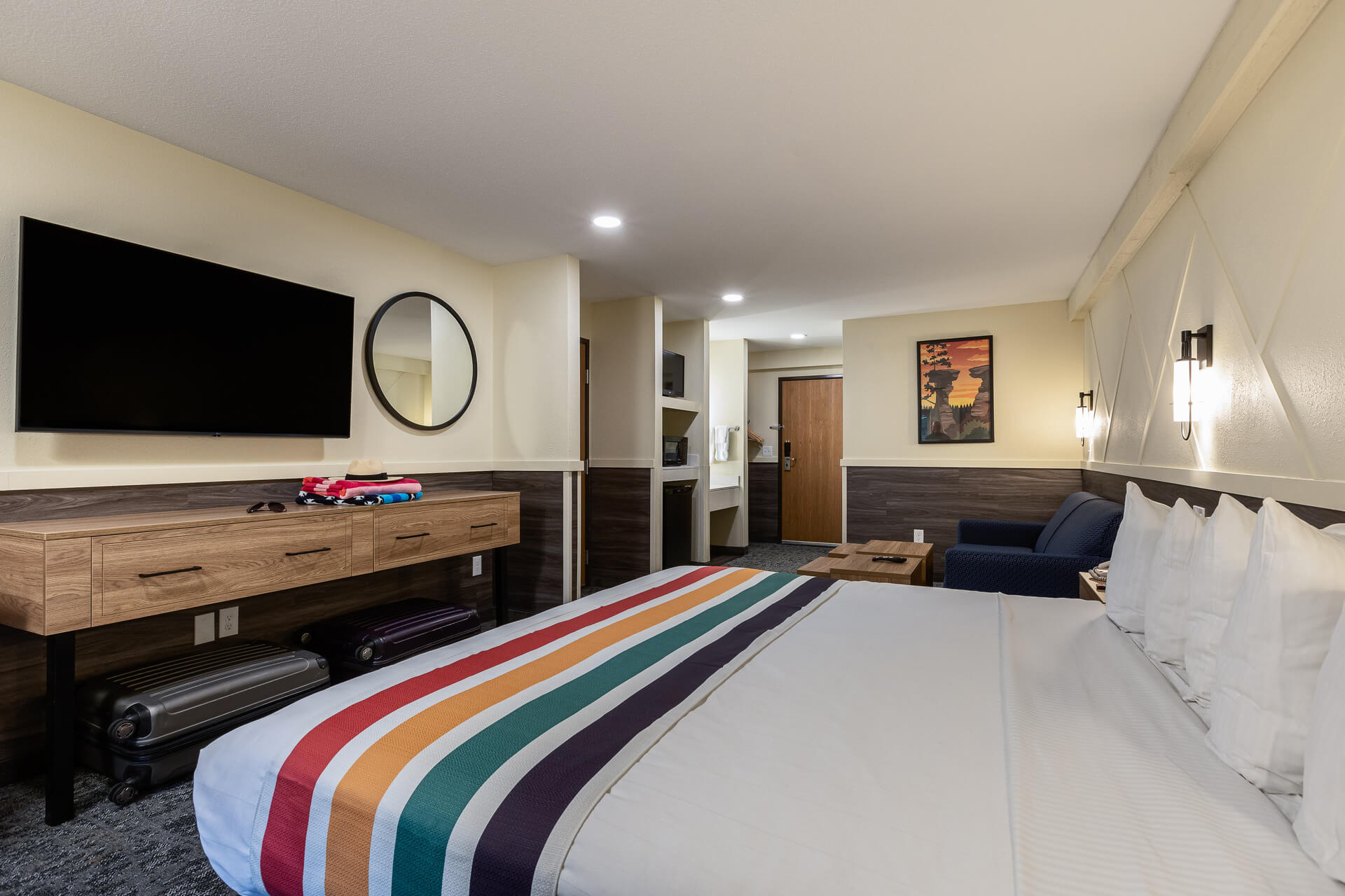 A hotel room with a king-size bed, a desk, a TV, and a sitting area.