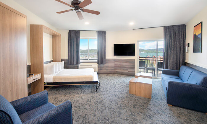 A wide view of a hotel suite with a bed, sofa, TV, and balcony.