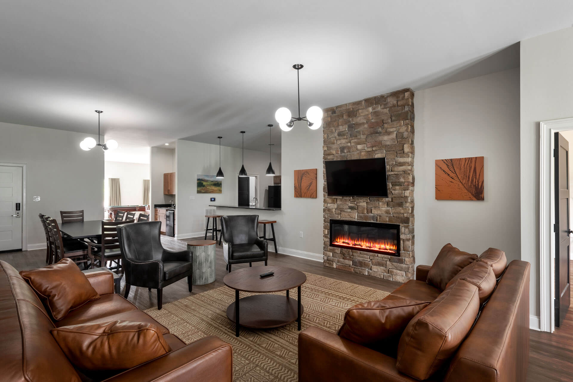 A wide shot of a spacious living room with a stone fireplace, leather sofas, a dining table, and a kitchenette.