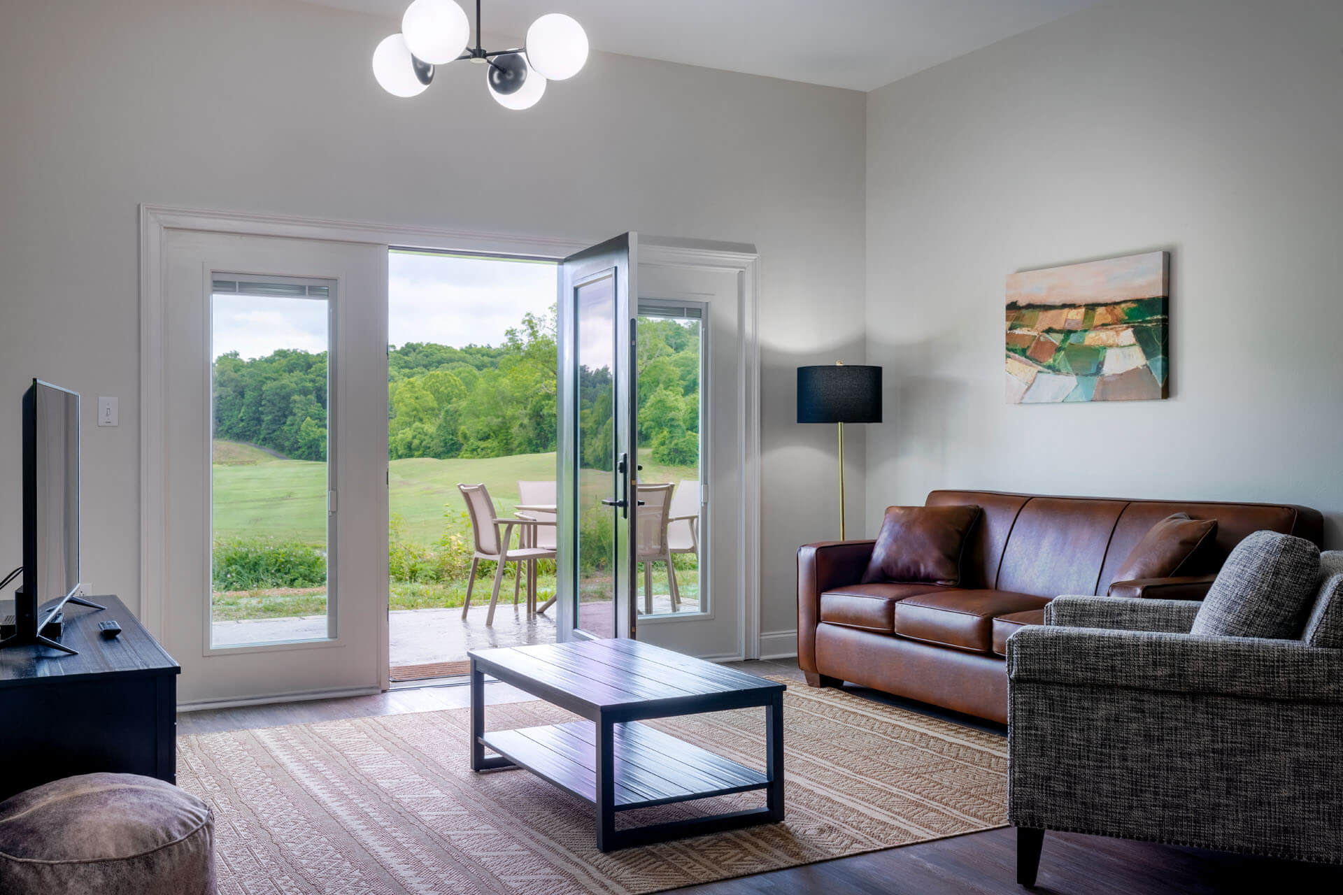 A wide view of a living room with a leather sofa, coffee table, and chairs, with sliding glass doors leading to an outdoor patio.