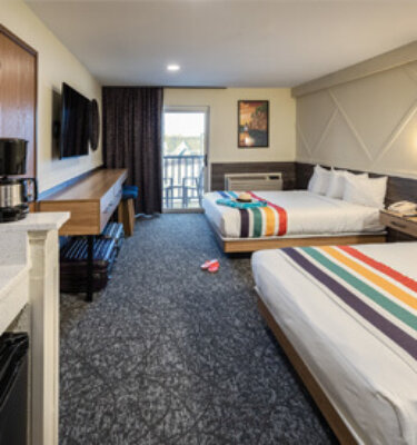 A hotel room with two beds, a balcony, a TV, and a coffee maker.