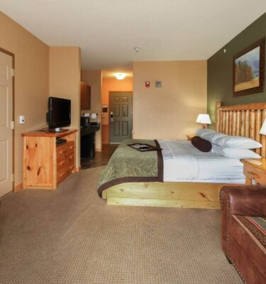 A wide view of a hotel room with a king-sized bed, wooden furniture, and a kitchenette.