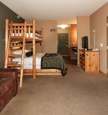 A wide view of a hotel room with a bunk bed, TV, and dresser.