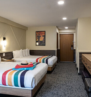 A hotel room with two beds, a doorway, and a small table.