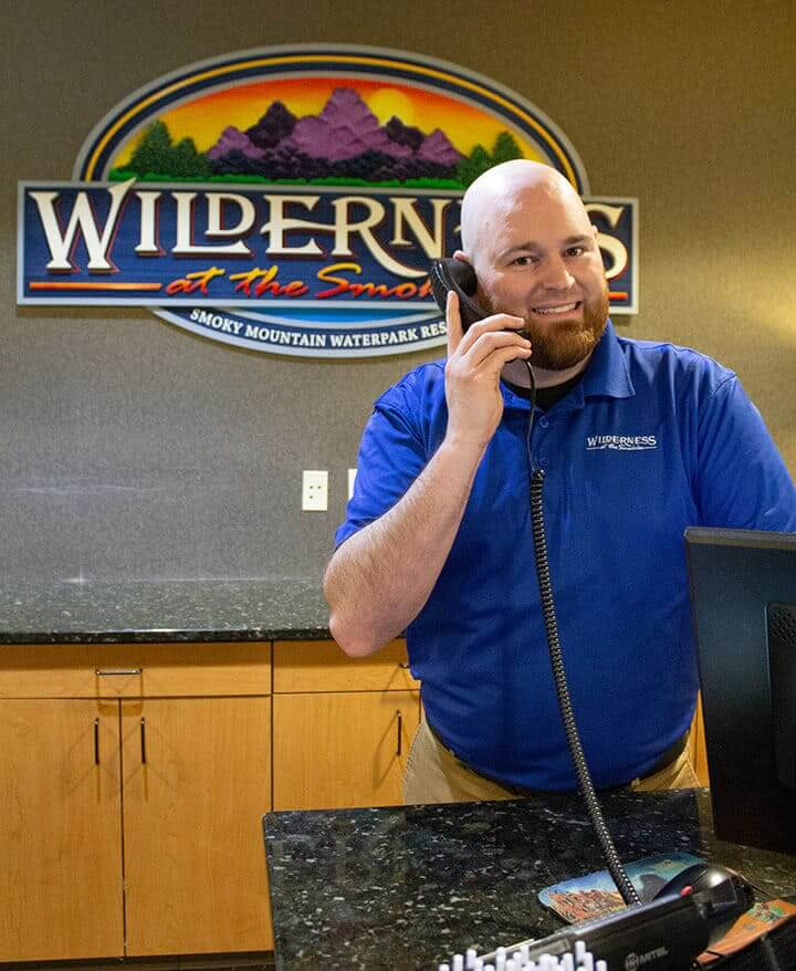 A man in a blue polo shirt is standing behind a front desk, talking on the phone.