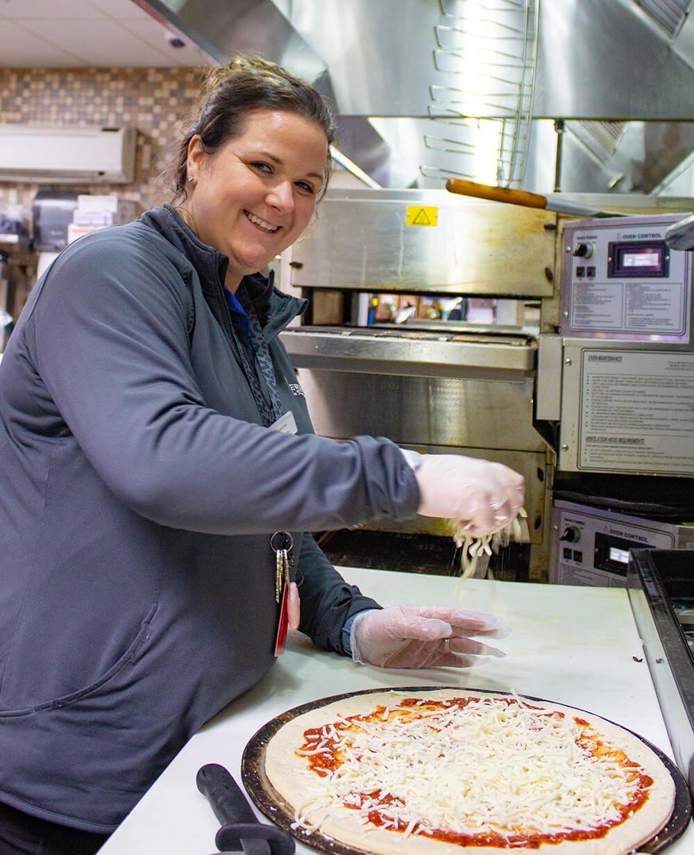 A woman in a kitchen preparing a pizza.
