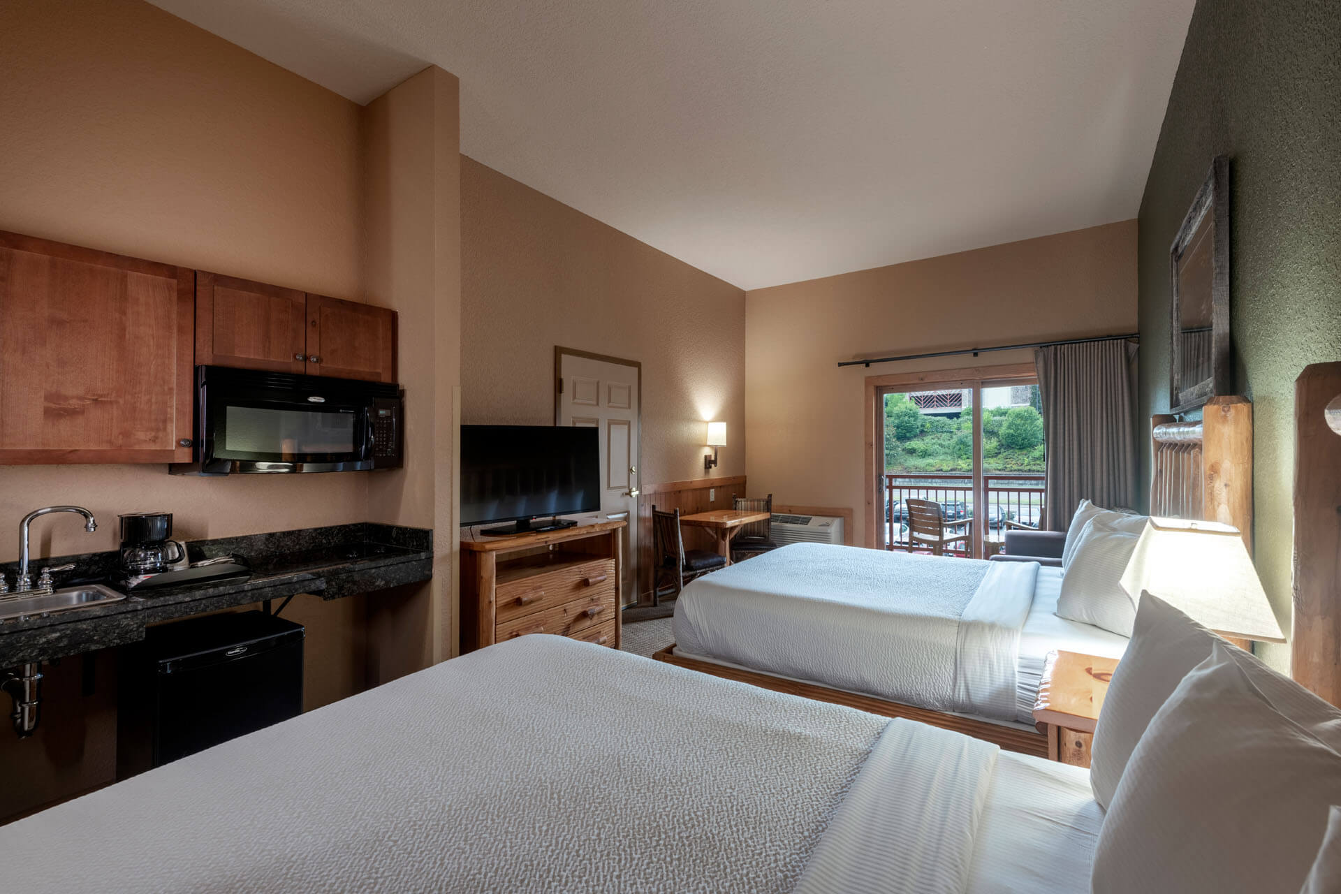 A hotel room with two beds, a kitchenette, and a balcony.