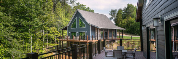A large house with a deck and fenced area surrounded by trees.