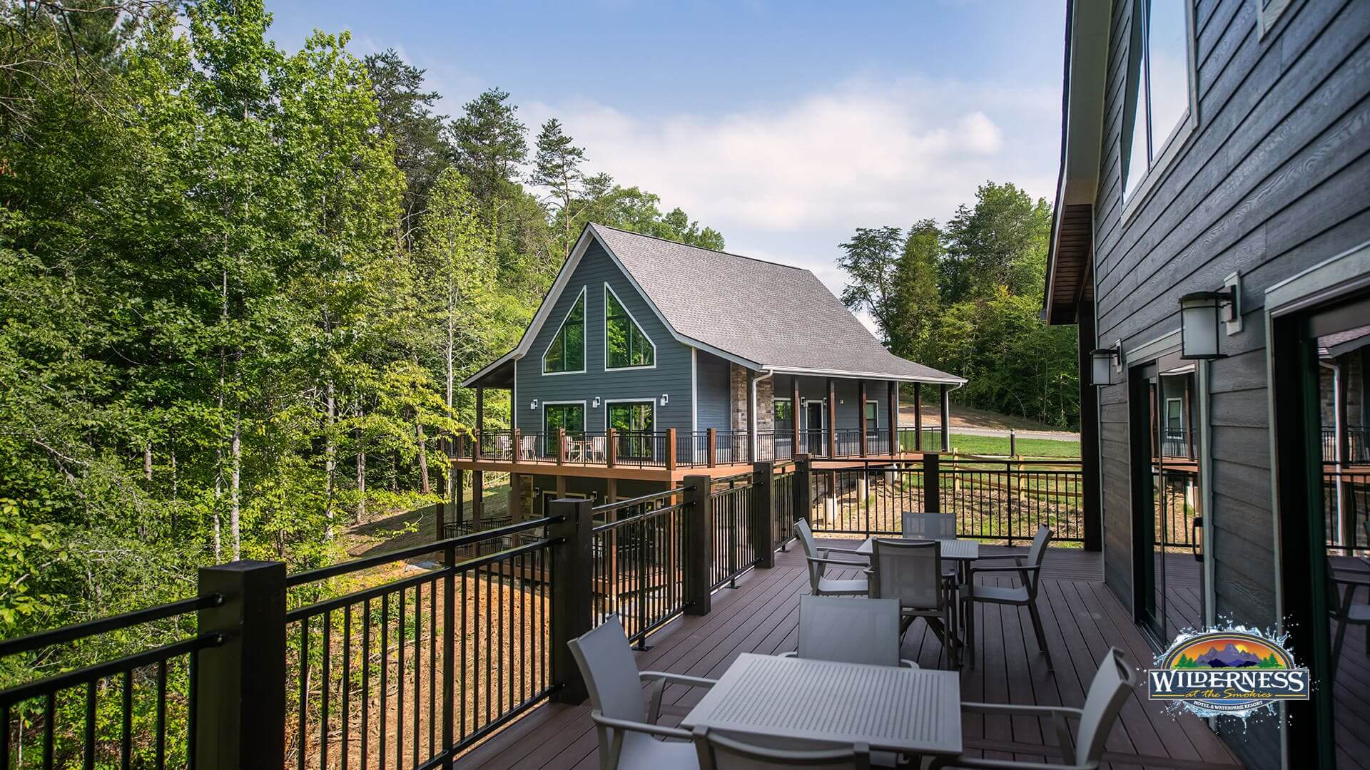 A wooden deck with outdoor furniture and a metal railing overlooking trees and a building.
