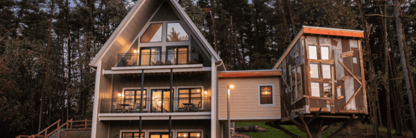 A multi-story cabin with balconies and a treehouse in a forest setting.