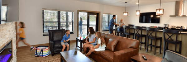 A large living room with a kitchenette, a fireplace, and a seating area with a family.
