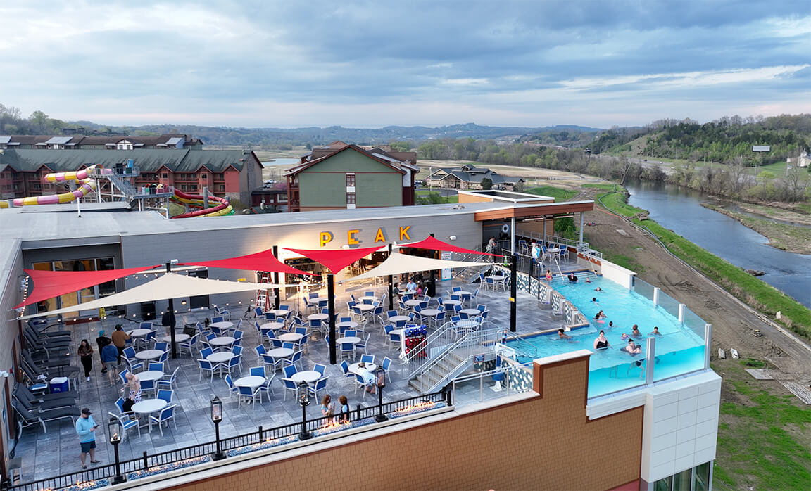 A rooftop bar and pool area with outdoor seating, umbrellas, and a mountain view.