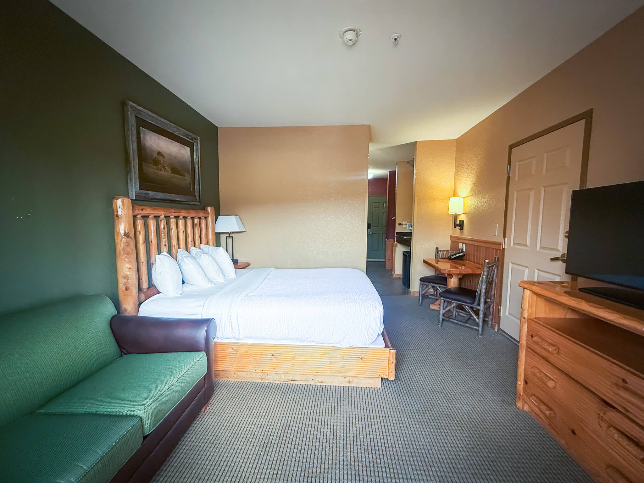 A wide view of a hotel suite with a large bed, green couch, wooden desk, and flat screen TV.